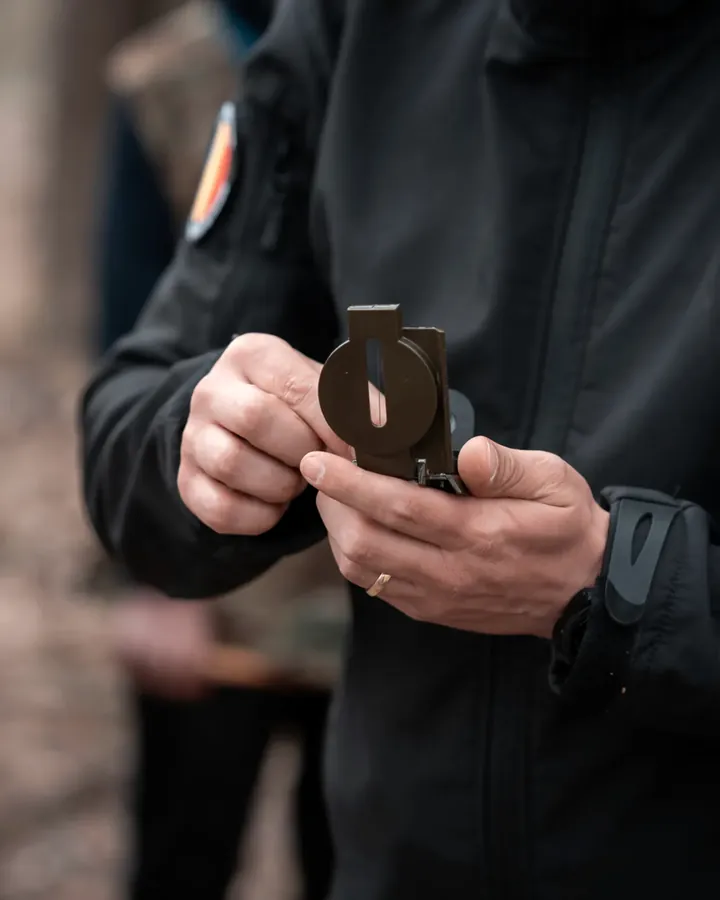 Mâinile unui instructor care deschide o busolă cu lupă pentru orientare în teren